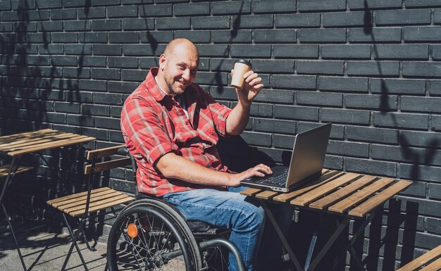 Freelancer with a physical disability in a wheelchair working at the street cafe