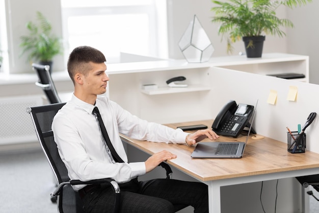 A freelancer with a shirt uses a laptop while sitting in the office and reading the news