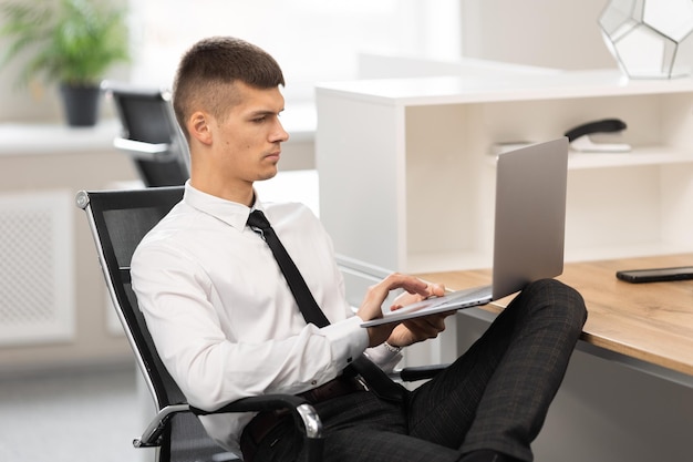 A freelancer with a shirt uses a laptop while sitting in the office and reading the news