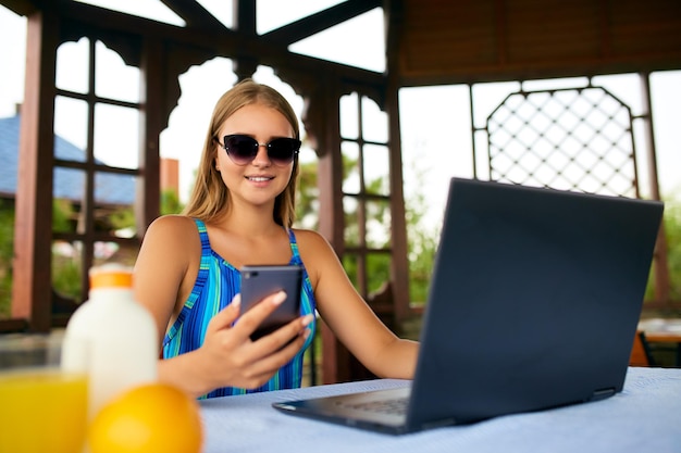 Freelancer woman sitting at garden house in tropical summer location and working with laptop