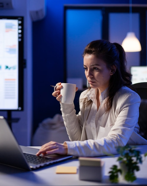 Freelancer woman with a cup of coffee tapping on business computer overworking at marketing project