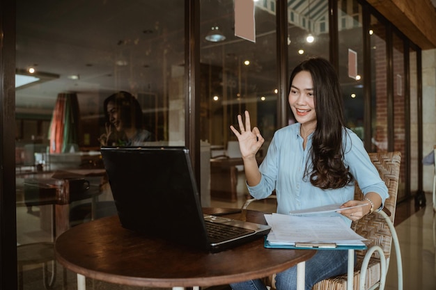 Freelancer woman working using laptop with okay hand gesture during online conference in co-working space