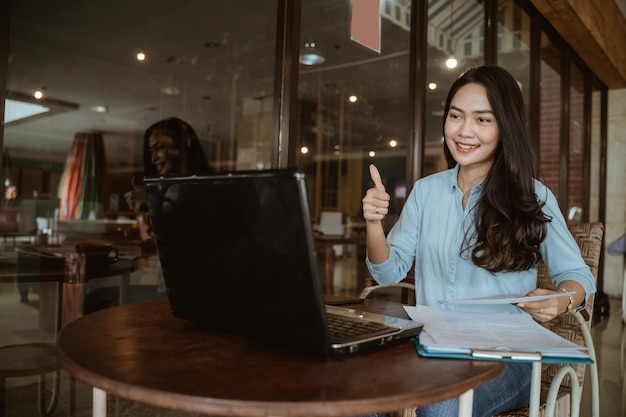 Freelancer woman working using laptop with thumbs up hand gesture during online conference in co-working space