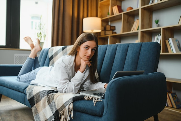 Freelancer working on laptop at home laying on comfortable beige sofa