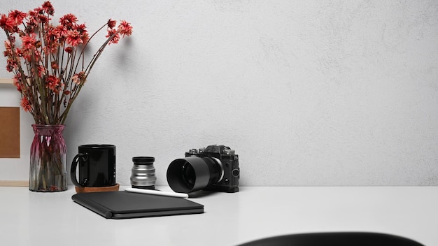 Posto di lavoro freelance con cornice per taccuino con fotocamera e vaso di fiori sul tavolo bianco