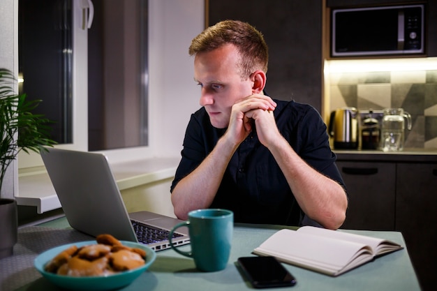 A freelancer works from home in the kitchen and using a laptop. Successful man working with a laptop and reading good news. Handsome successful entrepreneur sits and works in his modern home.
