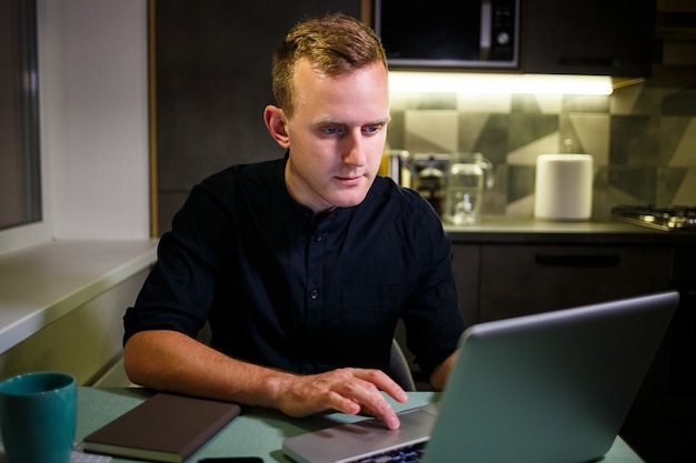 Un libero professionista lavora da casa in cucina e utilizzando un laptop. uomo di successo che lavora con un laptop e legge buone notizie. un bell'imprenditore di successo si siede e lavora nella sua casa moderna.