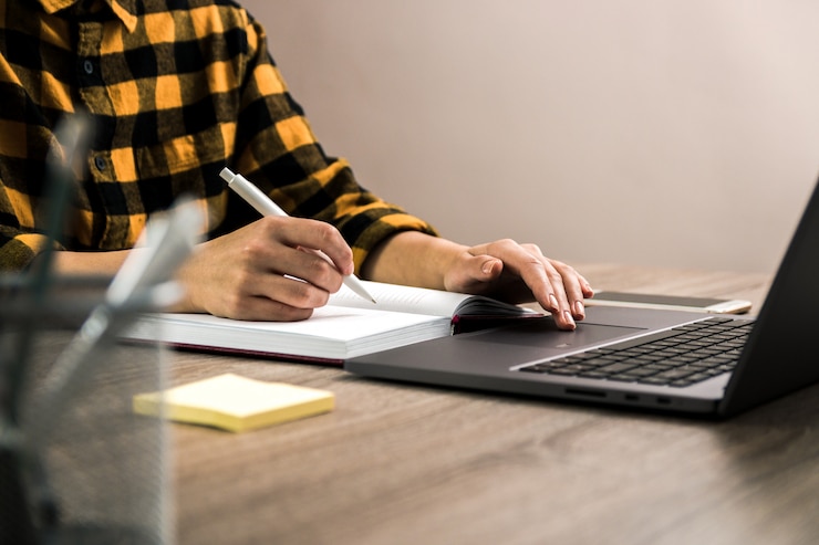 Photo freelancer in yellow shirt making notes in her notebook