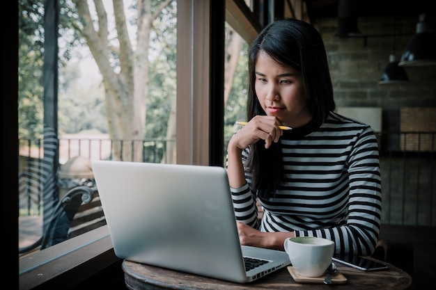 Freelancervrouw gebruikend haar laptop en kijkend laptop scherm terwijl het Planning van het denken concept in koffie.