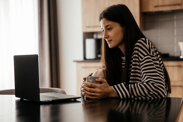 Freelancervrouw zit bij de tafel in het thuiskeukenkantoor en werkt op laptop Speels kind leidt af van het werk Kind maakt lawaai en vraagt aandacht van drukke moeder