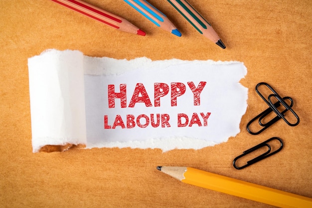 Freepik Happy Labour Day text under torn paper Coloured pencils and office supplies