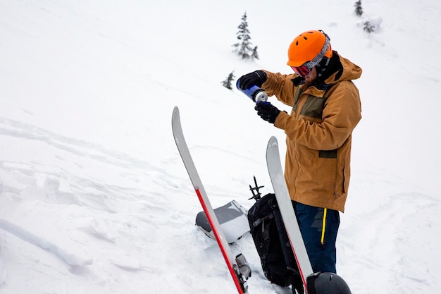 A freerider pours warm tea from a thermos while skiing outside