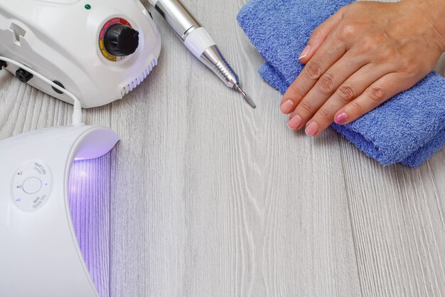 Frees, ingeschakeld led UV-lamp en een vrouwelijke hand op een handdoek op grijze achtergrond. Een set cosmetische hulpmiddelen voor professionele hardware-manicure. Bovenaanzicht