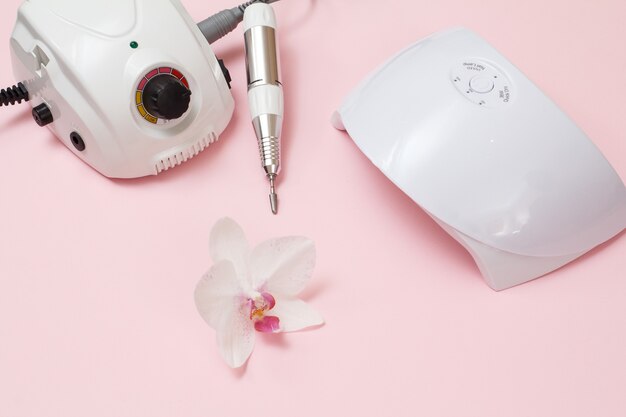 Frees, led UV-lamp en orchideebloem op een roze achtergrond. Een set cosmetische hulpmiddelen voor professionele hardware-manicure. Bovenaanzicht.