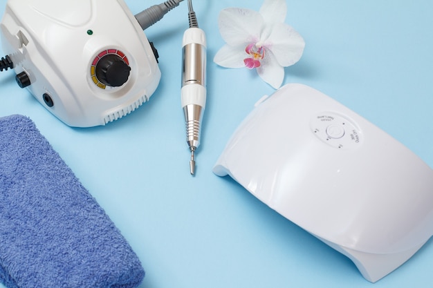 Frees, led UV-lamp, handdoek en witte orchideebloem op blauwe achtergrond. Een set cosmetische hulpmiddelen voor professionele hardware-manicure. Bovenaanzicht.