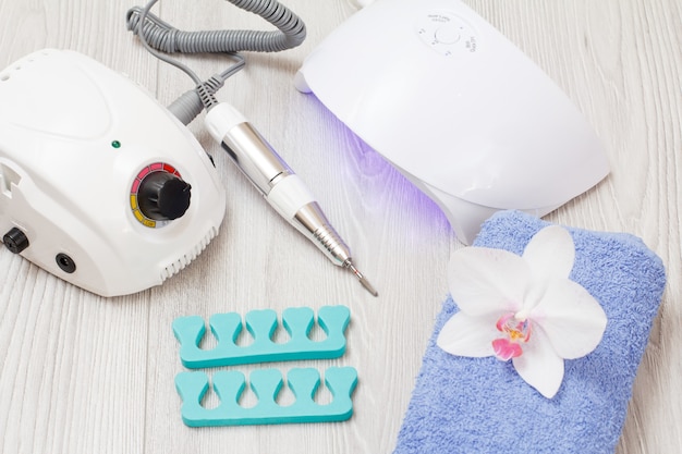 Frees, led UV-lamp, teenscheiders en handdoek met witte orchideebloem op grijze houten ondergrond. Een set cosmetische hulpmiddelen voor professionele hardware-manicure. Bovenaanzicht