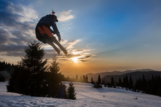 Freestyle extreme skier jumping from kicker in snowy mountains at orange sunset