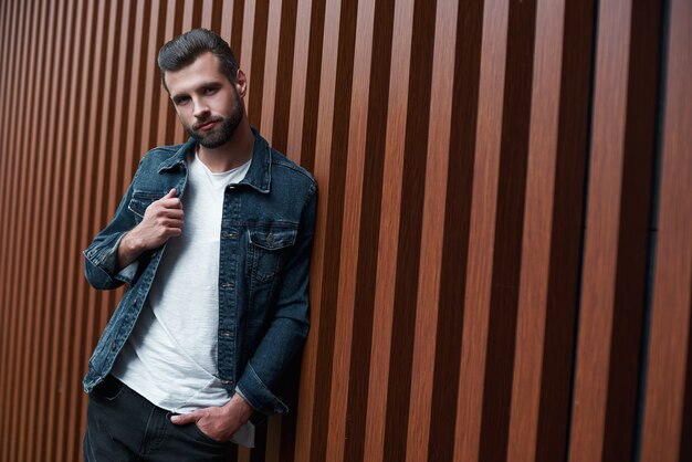 Freestyle young man standing leaning on wooden wall isolated looking camera smiling playful