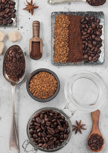Freeze dried instant coffee granules with ground coffee and beans in steel plate with glass jar and various spoons and scoops on white background.