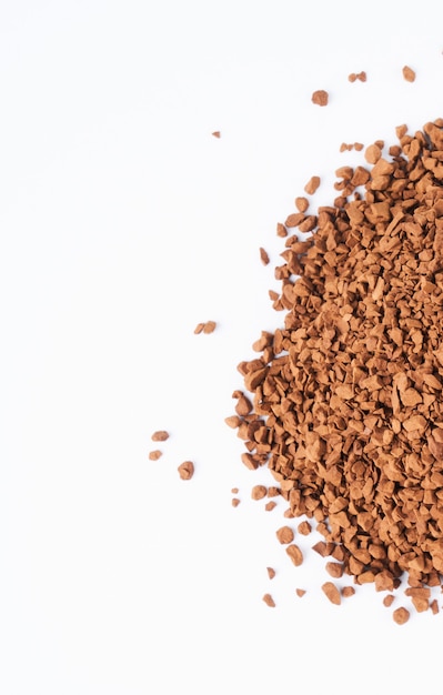 Freeze-dried instant coffee on white background close-up. Heap of powdered brown coffee product scattered on the table