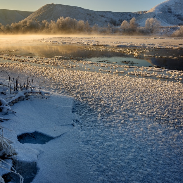 丘陵の土手と大きな流氷からの凍る川