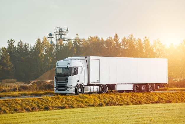 A freight truck transports a container on a motorway Logistic in Europe concept Driving a cargo semitruck on a highway with a beautiful red sun setting behind