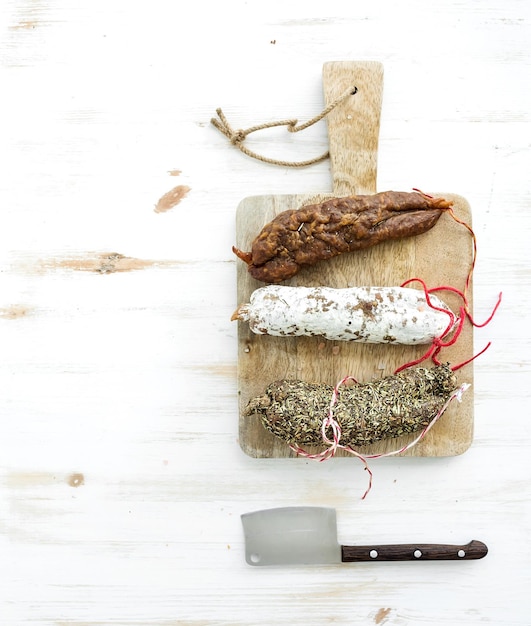 French alsacian smoked salamis on rustic wooden chopping board over white backdrop top view