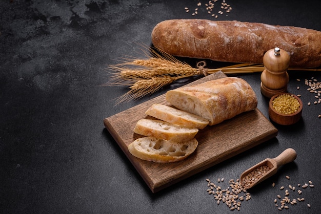 French baguette bread sliced on a wooden cutting board against a dark concrete background