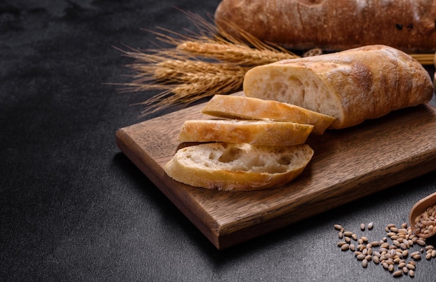 Французский багетный хлеб, нарезанный на деревянной разделочной доске на темном бетонном фоне
