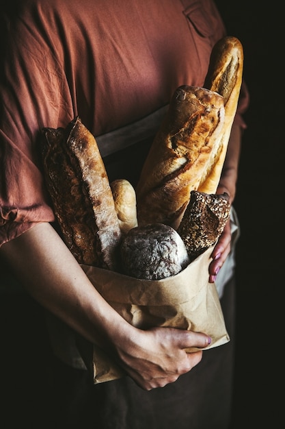 Foto baguette francesi in mani femminili su sfondo nero. dolci fatti in casa