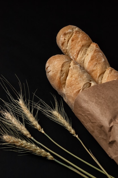 French baguettes in a paper bag and ears of wheat on a dark table