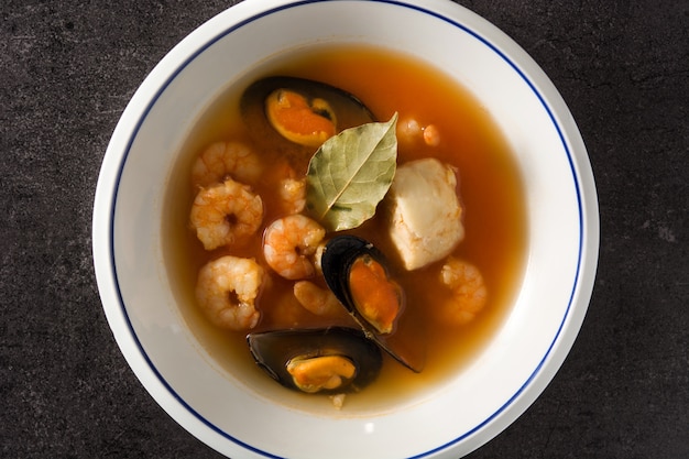 French bouillabaisse soup in white plate on black background. Top view