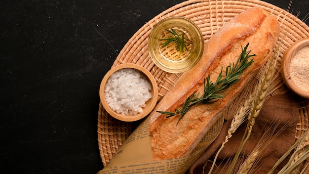 Foto pane francese o baguette e una tazza di farina e sale su un piatto di legno sul concetto di panetteria da tavola nera