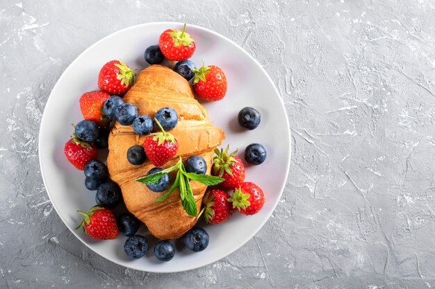 French breakfast, fresh croissant with strawberries and blueberries.