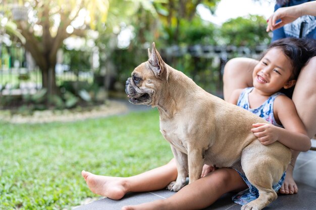 French bulldog sitting on little girl\'s lap and smiling at\
camera.