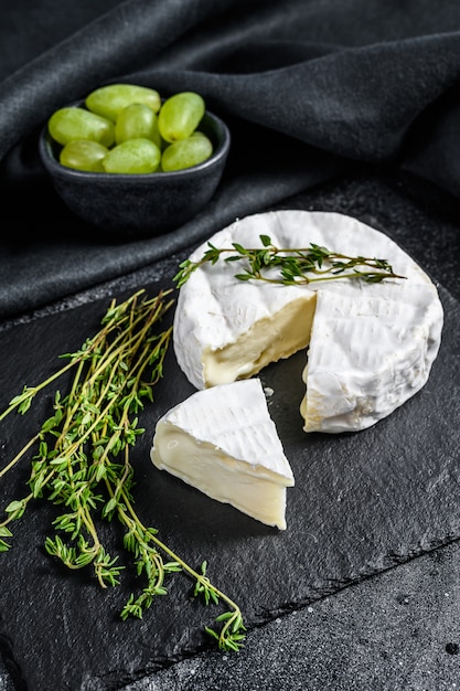 Foto camembert francese con uva. sfondo nero. vista dall'alto