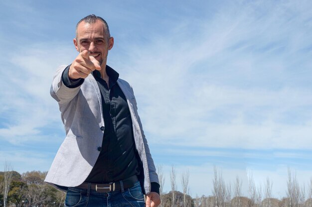 French caucasian businessman with beard and business clothes standing outdoors happy smiling pointing with finger and looking at camera sky background with copy space