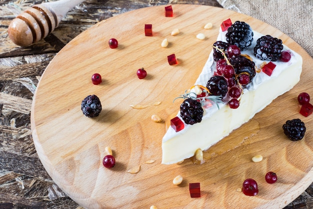 French cheese brie, camambert with honey, marmalade and pine nuts on wooden cheese board. 