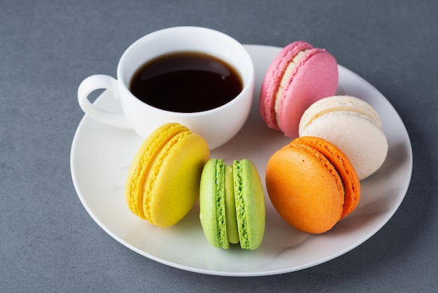 French colored macaroons with white cup of coffee on grey background