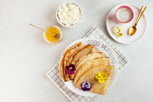 写真 フランスのクレープ、花で飾られたパンケーキ、カプチーノと蜂蜜のマグカップ。朝食、デザートのコンセプトです。