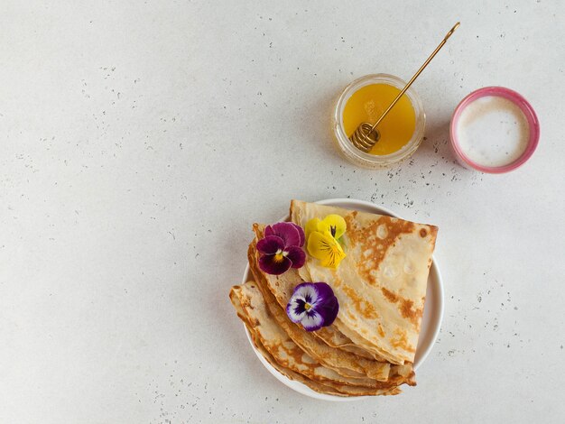 フランスのクレープ、花で飾られたパンケーキ、カプチーノと蜂蜜のマグカップ