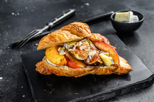 French croissant with bree cheese, peach and figs. Black wooden background.