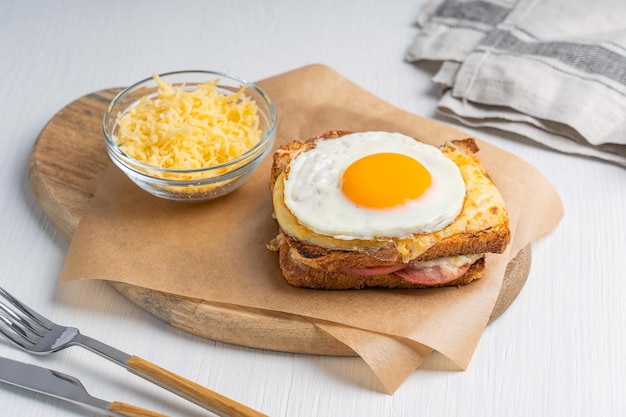 French croque madame hot sandwich baked with cheese and ham served on paper on cutting board