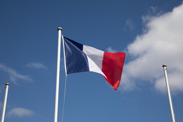 French flag at the top of a mast floats in the wind with two other empty masts for mockup country flags on sky