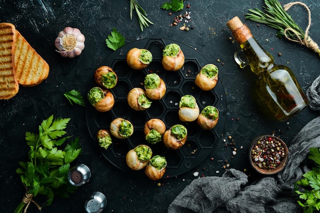 French food. Baked snails with pesto sauce on a black stone background. Top view. Free space for your text.