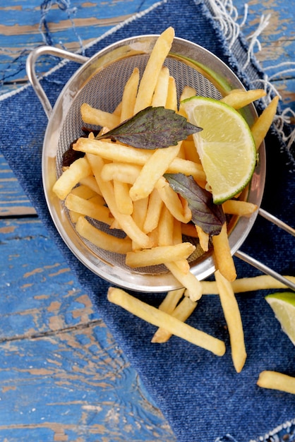 French fried potatoes in metal colander with sauce on wooden background