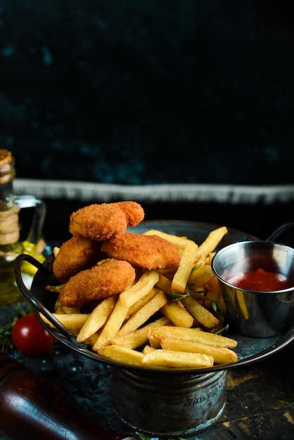 French fries and chicken nuggets with sauce on a metal plate on rustic wooden background Fast food concept