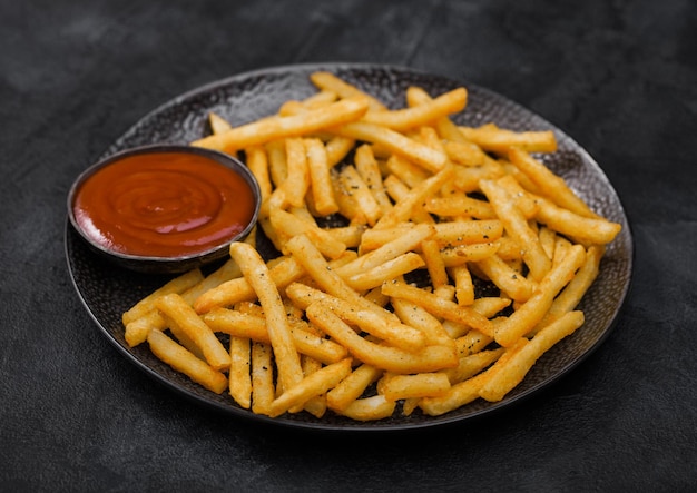 Patatine fritte con ketchup in lamiera nera su sfondo scuro del tavolo vista dall'alto