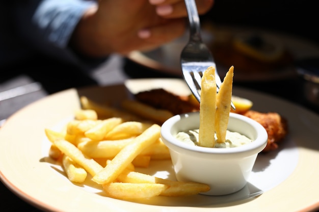 French fries on a fork in sauce next to meat chop