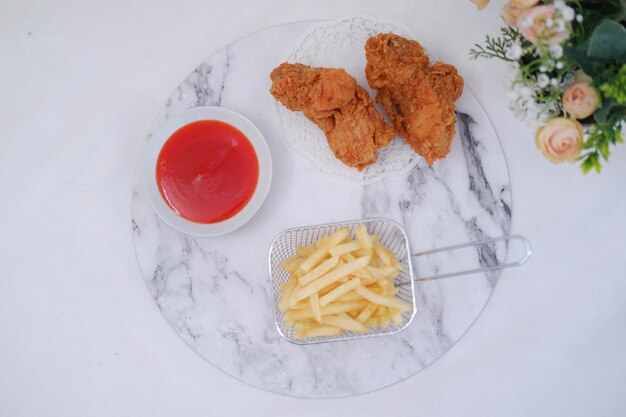 French fries fried chicken and ketchup on white marble table